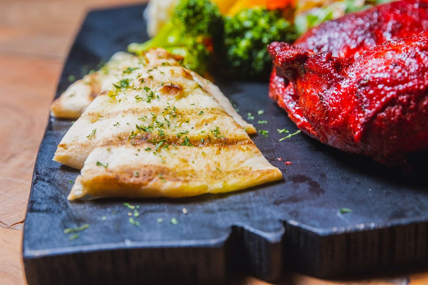 Grilled roti and jerk chicken with broccoli on a black board