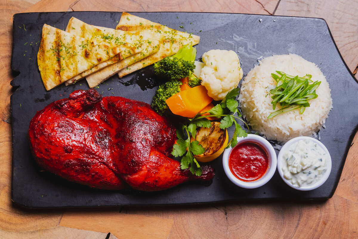 Tandoori chicken, flatbread, rice and sauces on a slate board for a restaurant opening