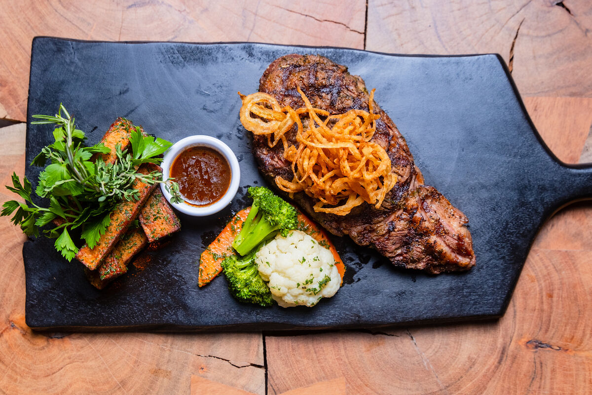 Grilled steak with crispy onions and sides on a black serving board